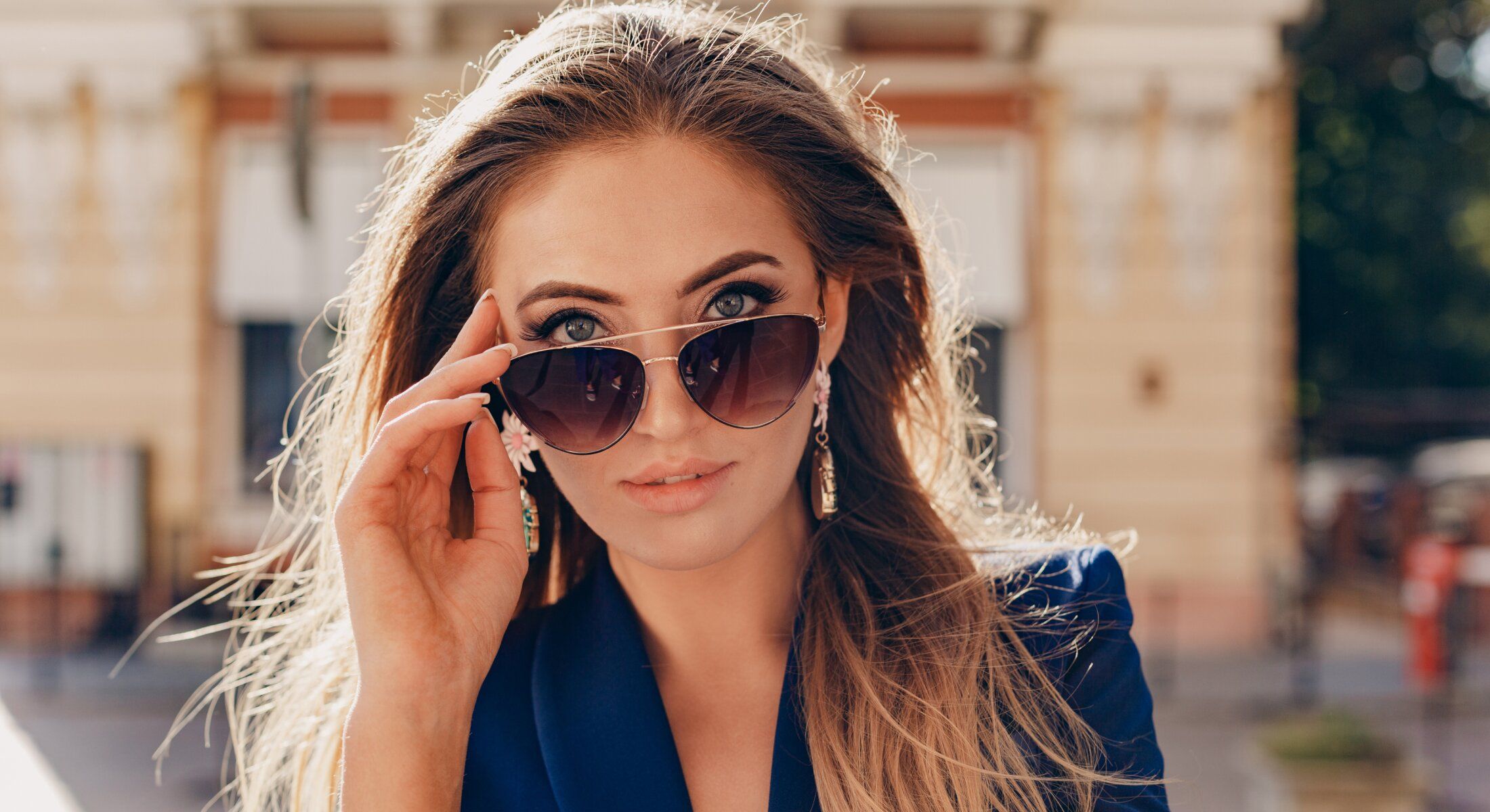 Woman adjusting sunglasses outdoors, stylish fashion look.